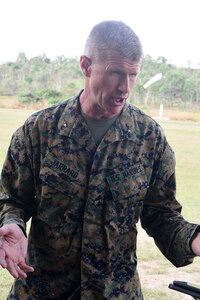 A person dressed in a military uniform uses hand gestures as he talks to someone outdoors.