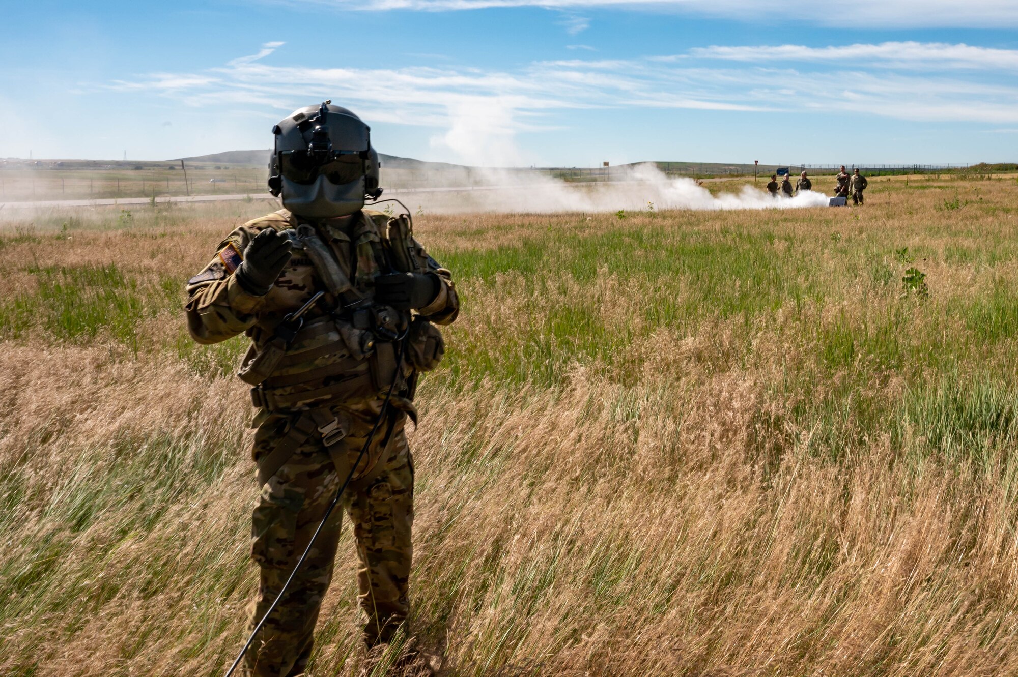 A man stands in a field with people and smoke in the background.