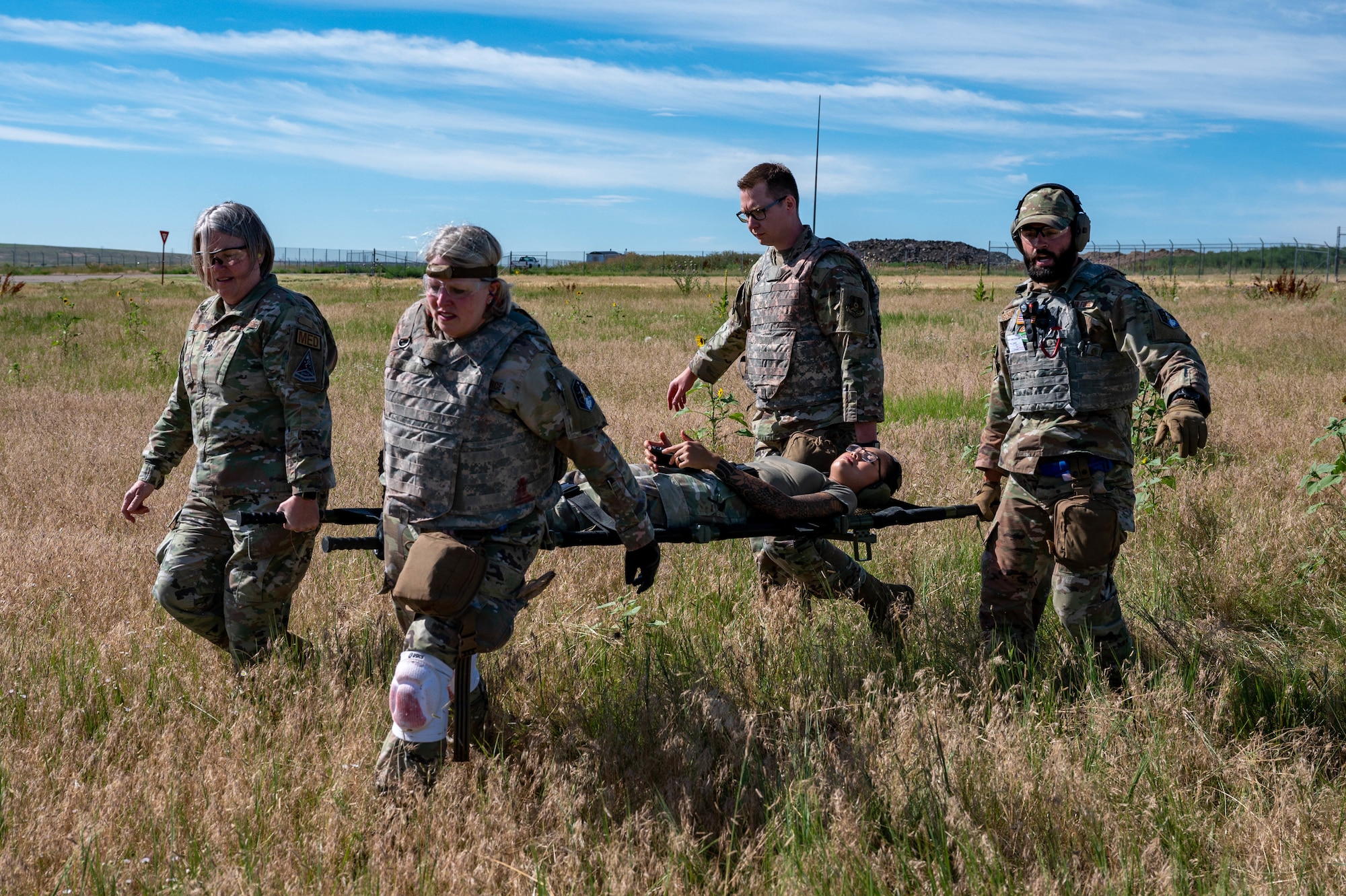 Four people carry a woman in a stretcher across a field.