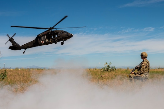  Man watches helicopter take off in large field.