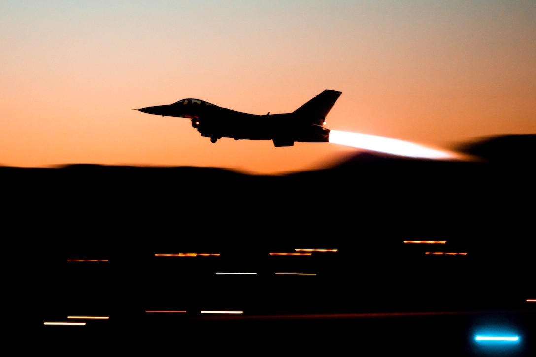 A fighter jet flies across an orange sky.