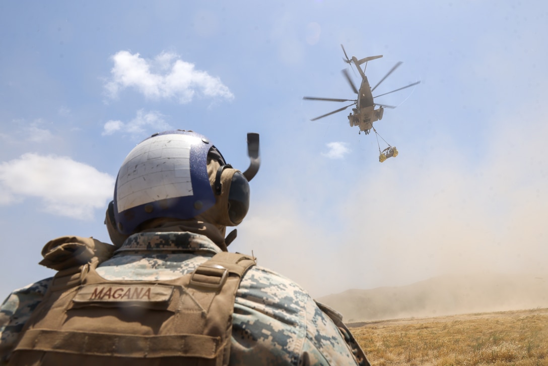 U.S. Marine Corps Lance Cpl. Diego Maganagarcia, a landing support specialist assigned to Combat Logistics Battalion 15, Combat Logistics Regiment 17, 1st Marine Logistics Group, monitors a Polaris MRZR, an ultra-light turbo diesel combat vehicle, hooked beneath a CH-53E Super Stallion attached to Marine Heavy Helicopter Squadron (HMH) 361, Marine Aircraft Group 16, 3rd Marine Aircraft Wing, during external lift operations at Marine Corps Base Camp Pendleton, California, May 9, 2023. CLB-15 and HMH-361 worked together to test an innovative lift method utilizing wheel nets to inform publication and standard operating procedure development for the Marine Corps. (U.S. Marine Corps photo by Cpl. Aidan Hekker)