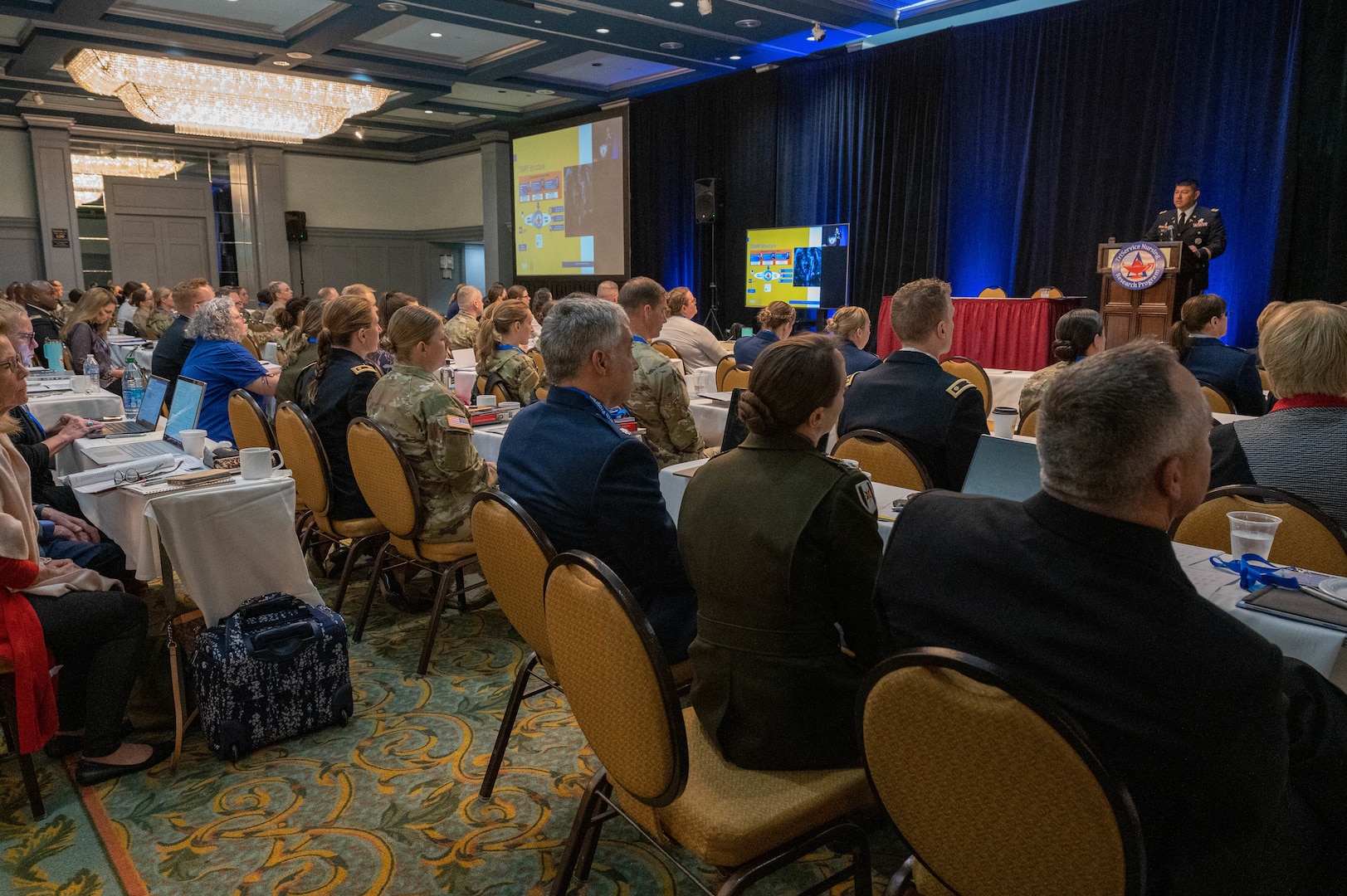 The TriService Nursing Research Program's annual Dissemination Course was held on April 4-6th, 2023, San Antonio, Texas. A room full of people sit while U.S. Army Executive Director Col. Young Yauger, PhD, CRNA, presents a power point slide to the attendees.