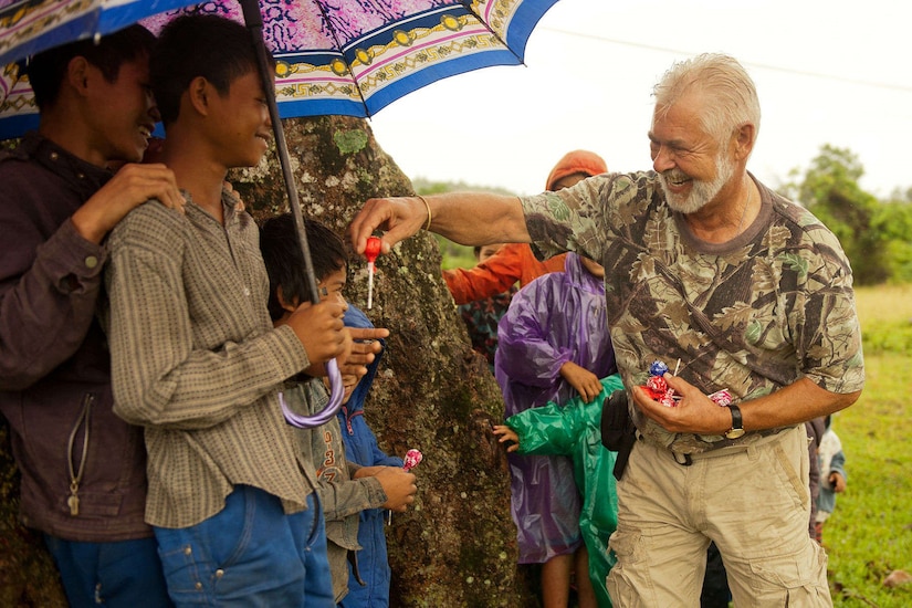 A smiling man hands candy to a child under an umbrella.