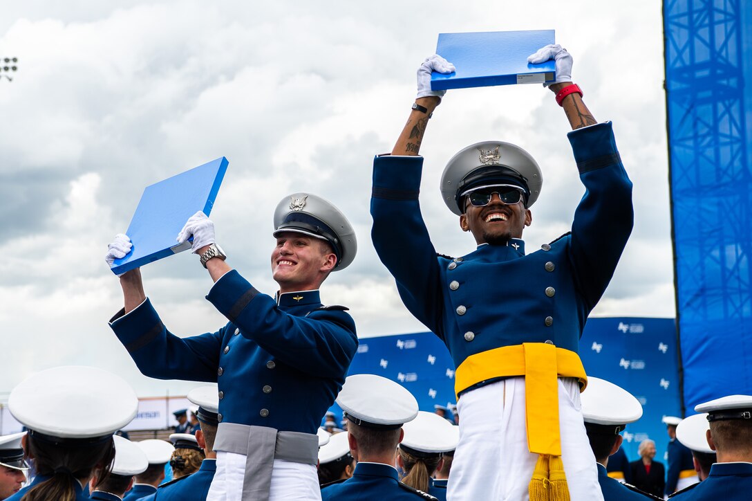 Two smiling Air Force cadets hold up skinny blue boxes in an outdoor space.