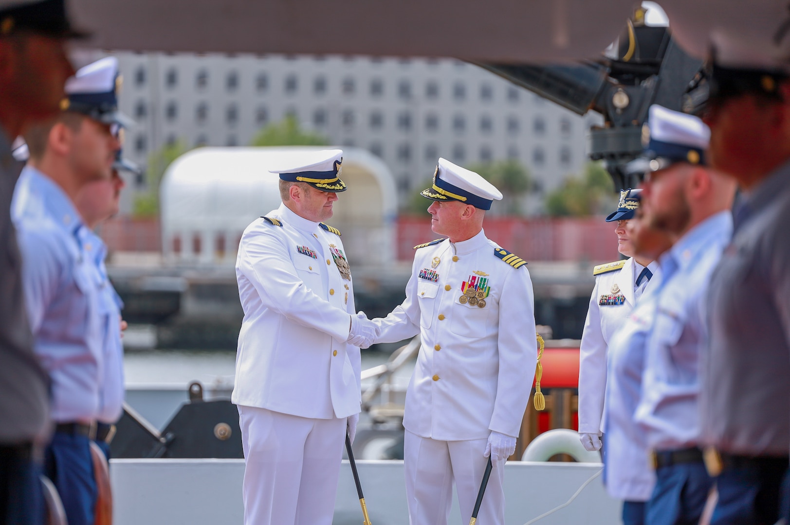 Capt. Justin Matthew Carter (left) shakes the hand of Capt. Matthew T. Brown (right) in front of USCGC Hamilton's (WMSL 753) crew as they arrive as the official party for the unit's change of command ceremony, June 1, 2023, at the Federal Law Enforcement Training Center in North Charleston, South Carolina. The change of command ceremony marks a transfer of total responsibility and authority from one individual to another. (U.S. Coast Guard photo by Ensign Ray Corniel)