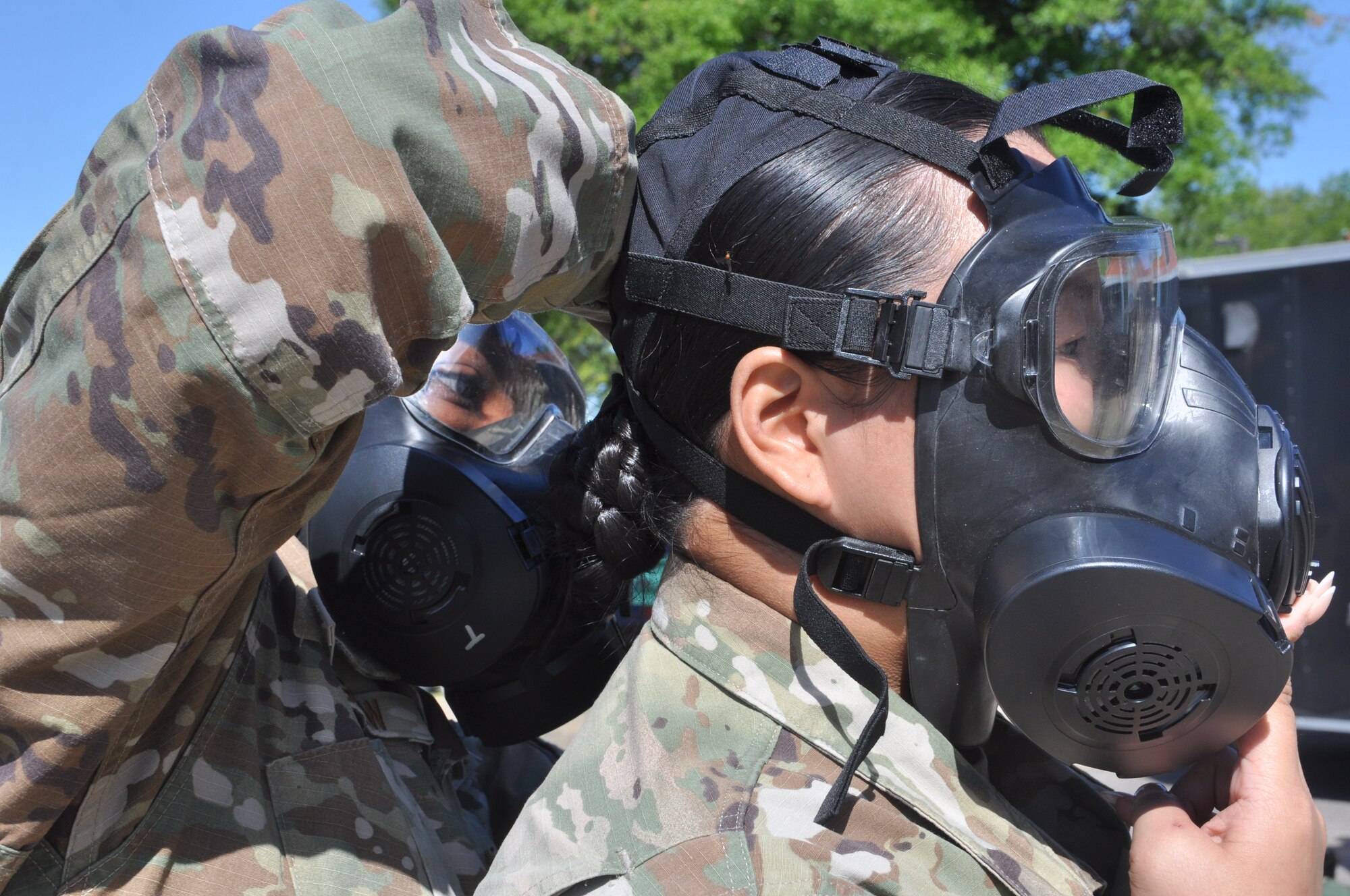 a woman helps another woman don a gas mask