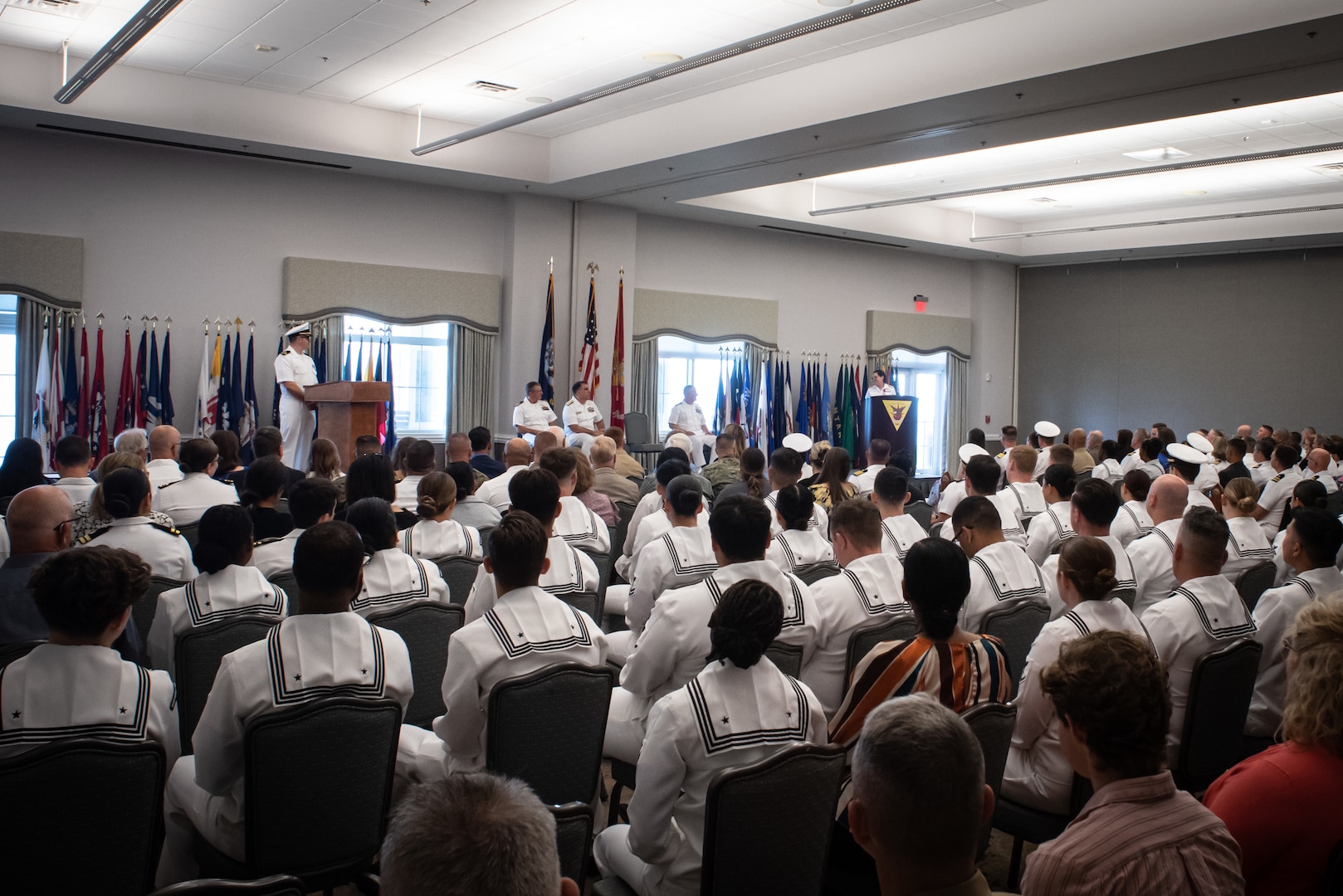 Capt. Elizabeth Adriano, right, at podium, gives her remarks during the Naval Health Clinic Cherry Point change of command ceremony May 31, 2023 aboard Marine Corps Air Station Cherry Point.  Adriano relinquished command of the clinic to Capt. Sean Barbabella during the ceremony.