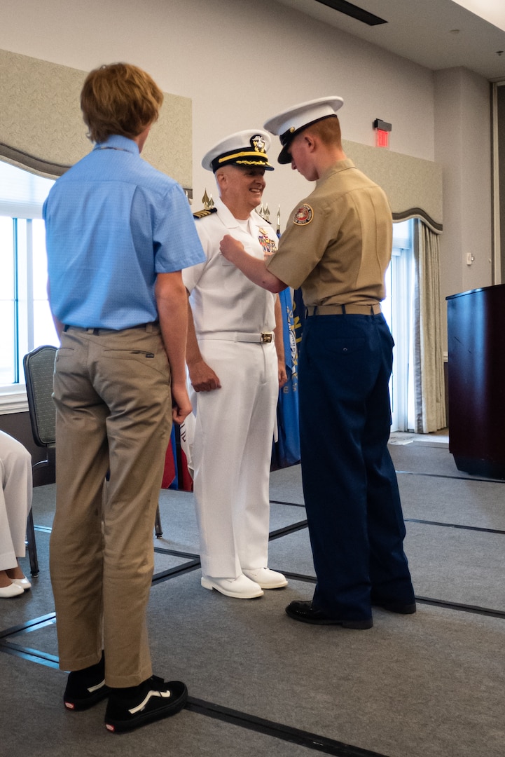 Sean Barbabella, a member of Navy Junior Reserve Officers Training Corps, pins the Command Ashore Insignia upon his father, Capt. Sean Barbabella, while his brother Matthew looks on during the Naval Health Clinic Cherry Point change of command ceremony May 31, 2023.  Barbabella assumed command of the clinic from Capt. Elizabeth Adriano during the ceremony.