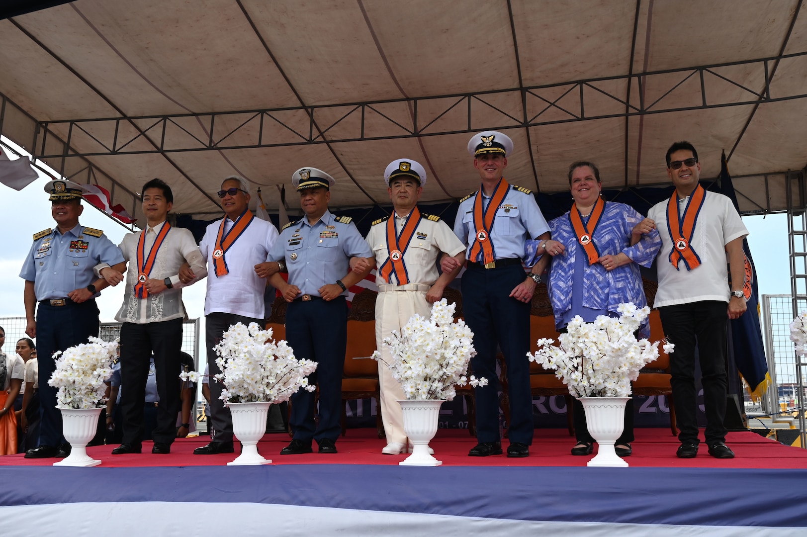 Members from the Philippine Coast Guard, Japan Coast Guard, U.S. Coast Guard and government officials from each country stand-arm and-arm with each other following the arrival of the U.S. Coast Guard Cutter Stratton (WMSL 752) and the Japan Coast Guard Vessel Akitsushima (PLH 32) to Manila, Philippines, for a tri-lateral engagement between the three coast guards, June 1, 2023. Stratton deployed to the Western Pacific under U.S. Navy 7th Fleet command to serve as a non-escalatory asset for the promotion of a rules-based order in the maritime domain by engaging with partner nations and allies in the region. (U.S. Coast Guard photo by Chief Petty Officer Matt Masaschi)