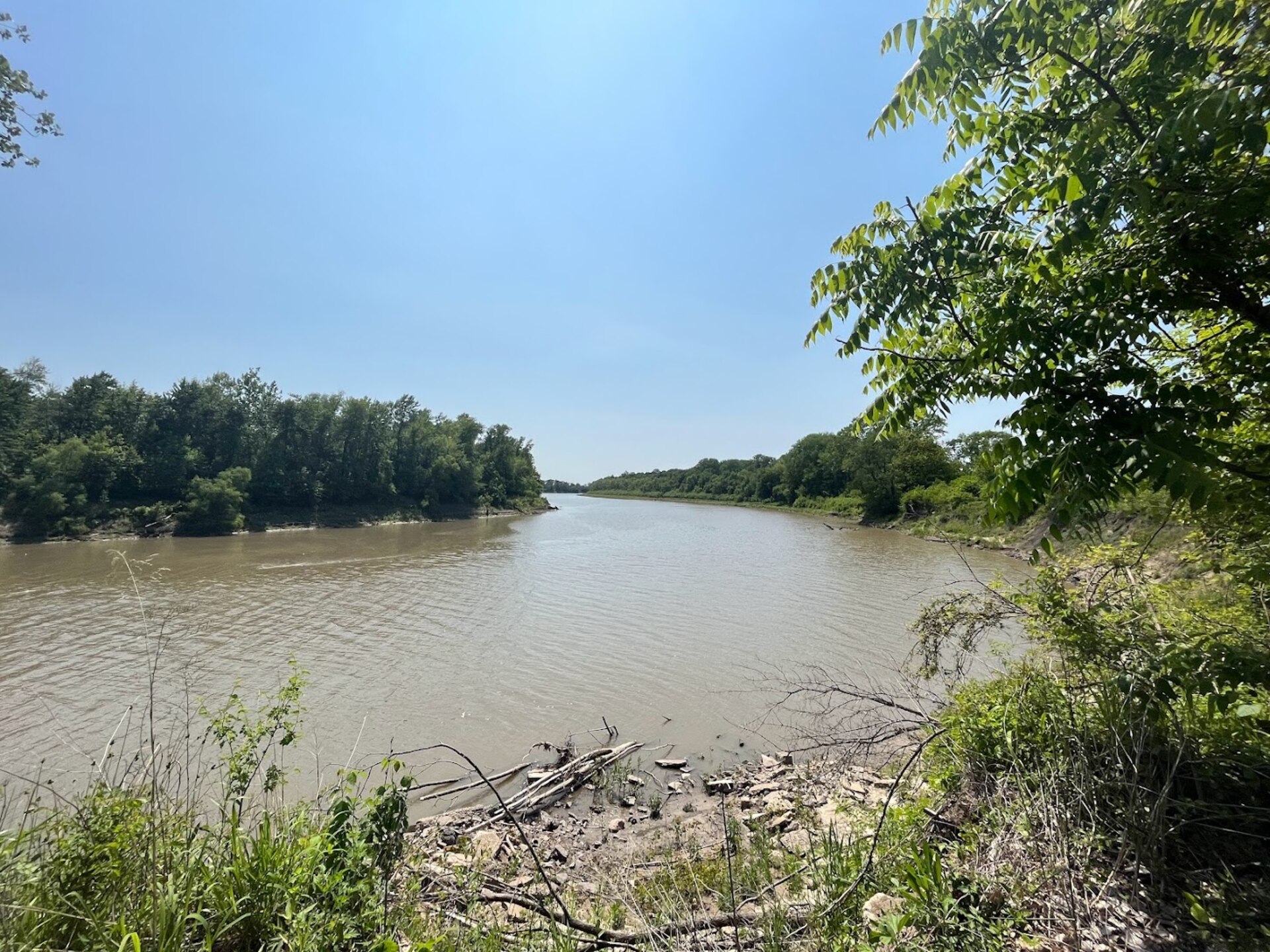 The Missouri River can be seen flowing with trees on either side and a blue sky in the background.