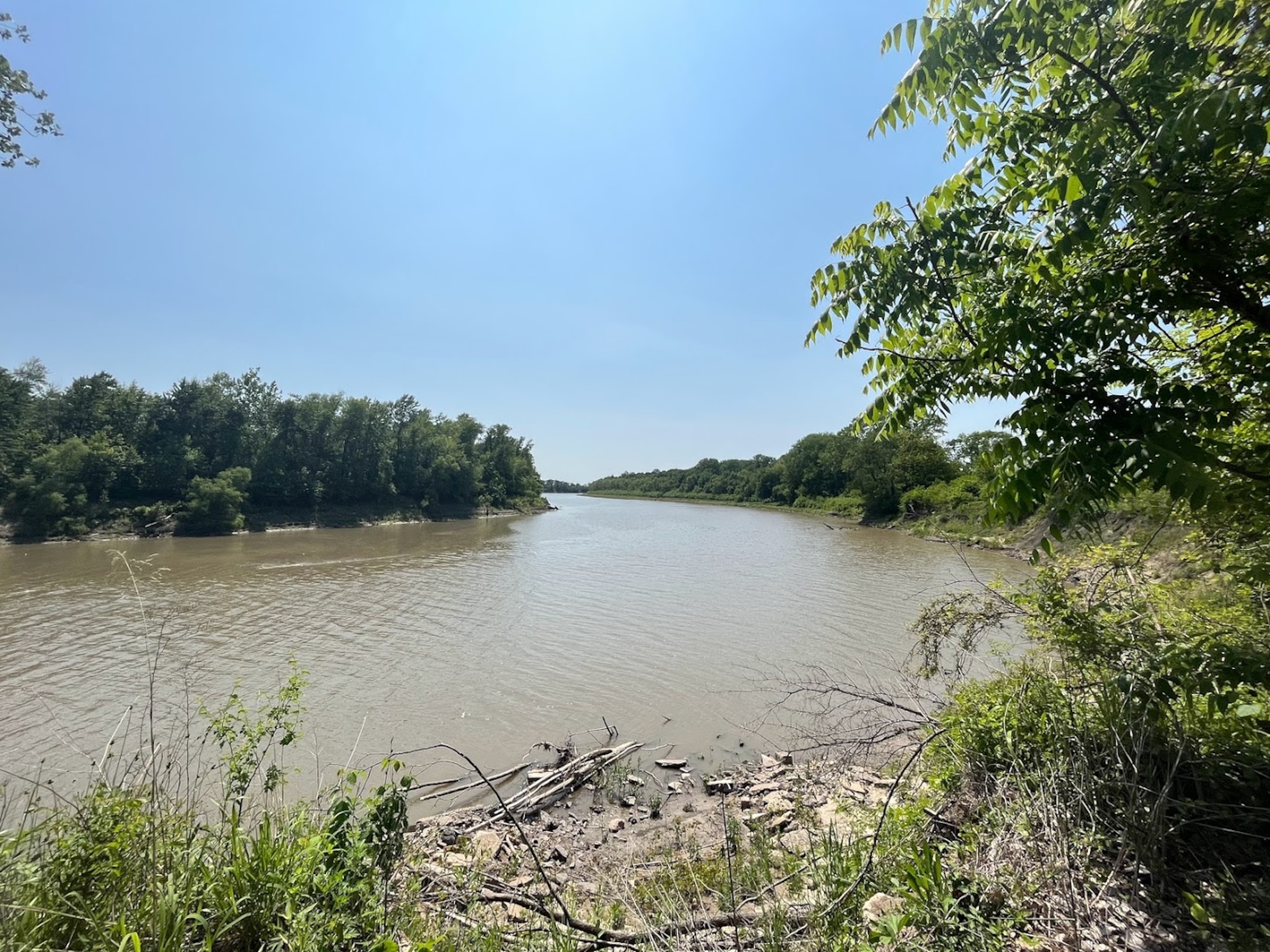 The Missouri River can be seen flowing with trees on either side and a blue sky in the background.