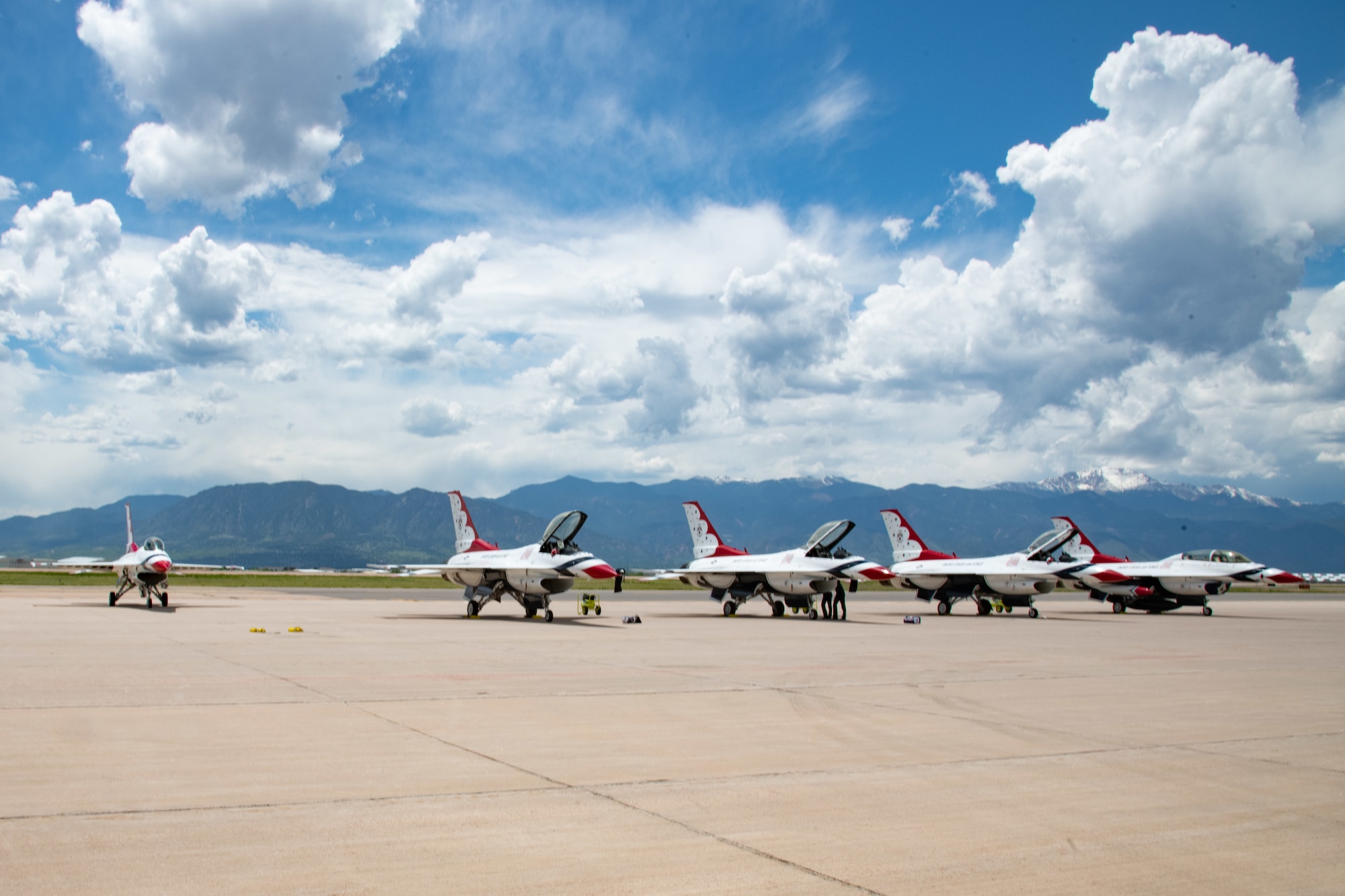 Five red, white and blue Air Force fighter jets sit on a runway in front of mountains.