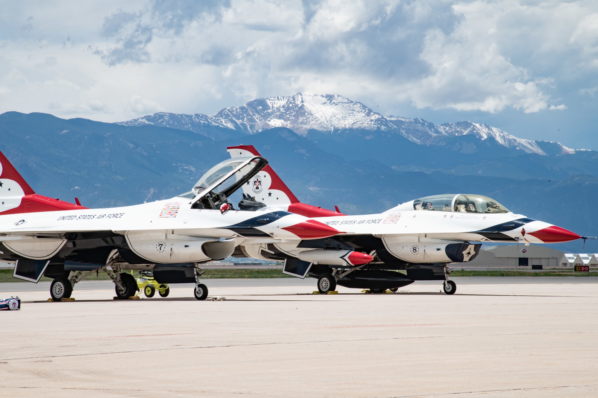 Two red, white and blue Air Force fighter jets sit on a flightline with a large snow-capped mountain in the background.