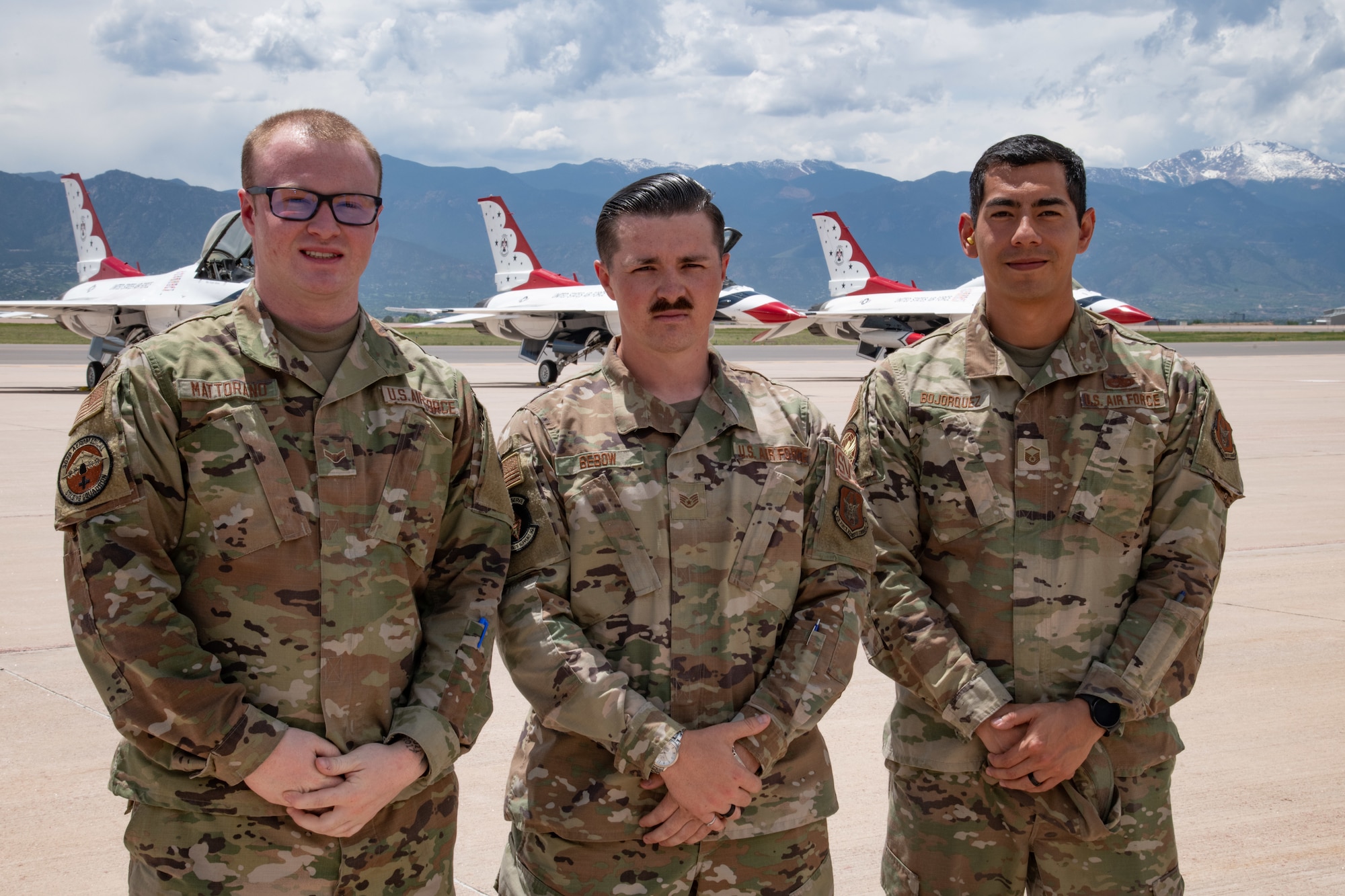 Three military members stand in front of red, white and blue fighter jets.