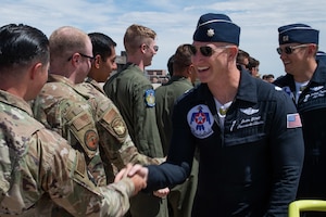 Air Force officer in Thunderbird flight suit shakes hands with an Airman wearing the Air Force OCP uniform.