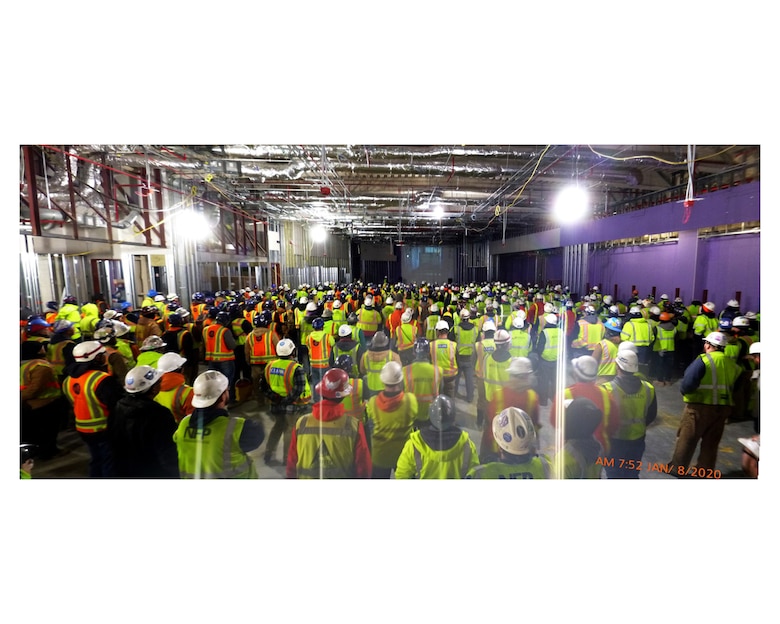 Contractor teammates wearing hard hats and construction vests stand together for a meeting.