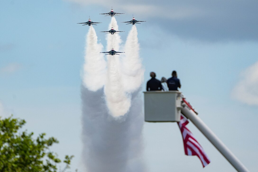 Military aircraft fly over people inside a cherry picker.