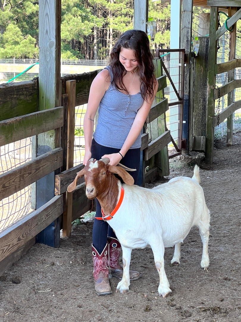 Girl in cowboy boots holding goat in a pen.