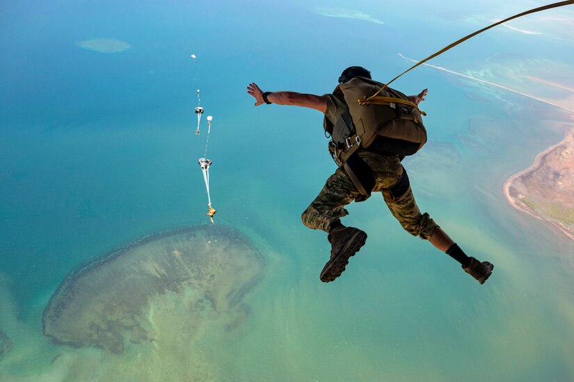 Air Force personnel free-fall with parachutes over a body of water as seen from above.