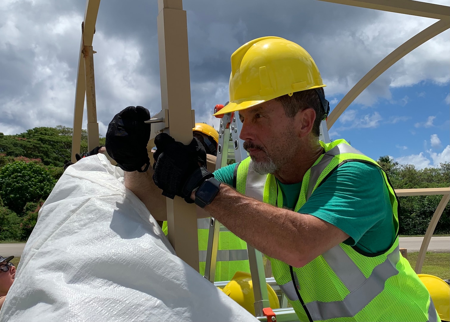 A man in a hardhat constructs a temporary shelter from metal poles.