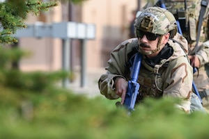 A male airman with a brown mustache holds a blue training rifle.