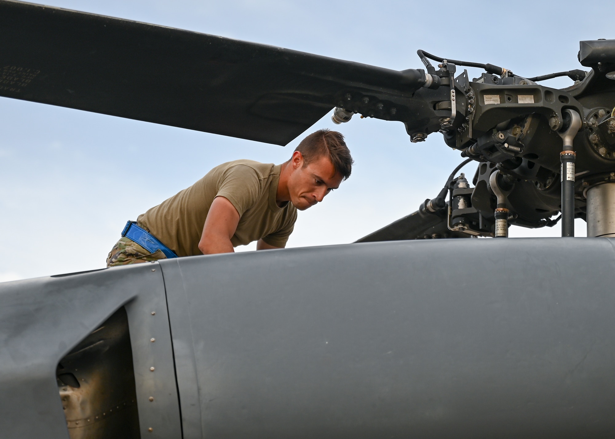 A man in a military uniform works on the top of a helicopter.