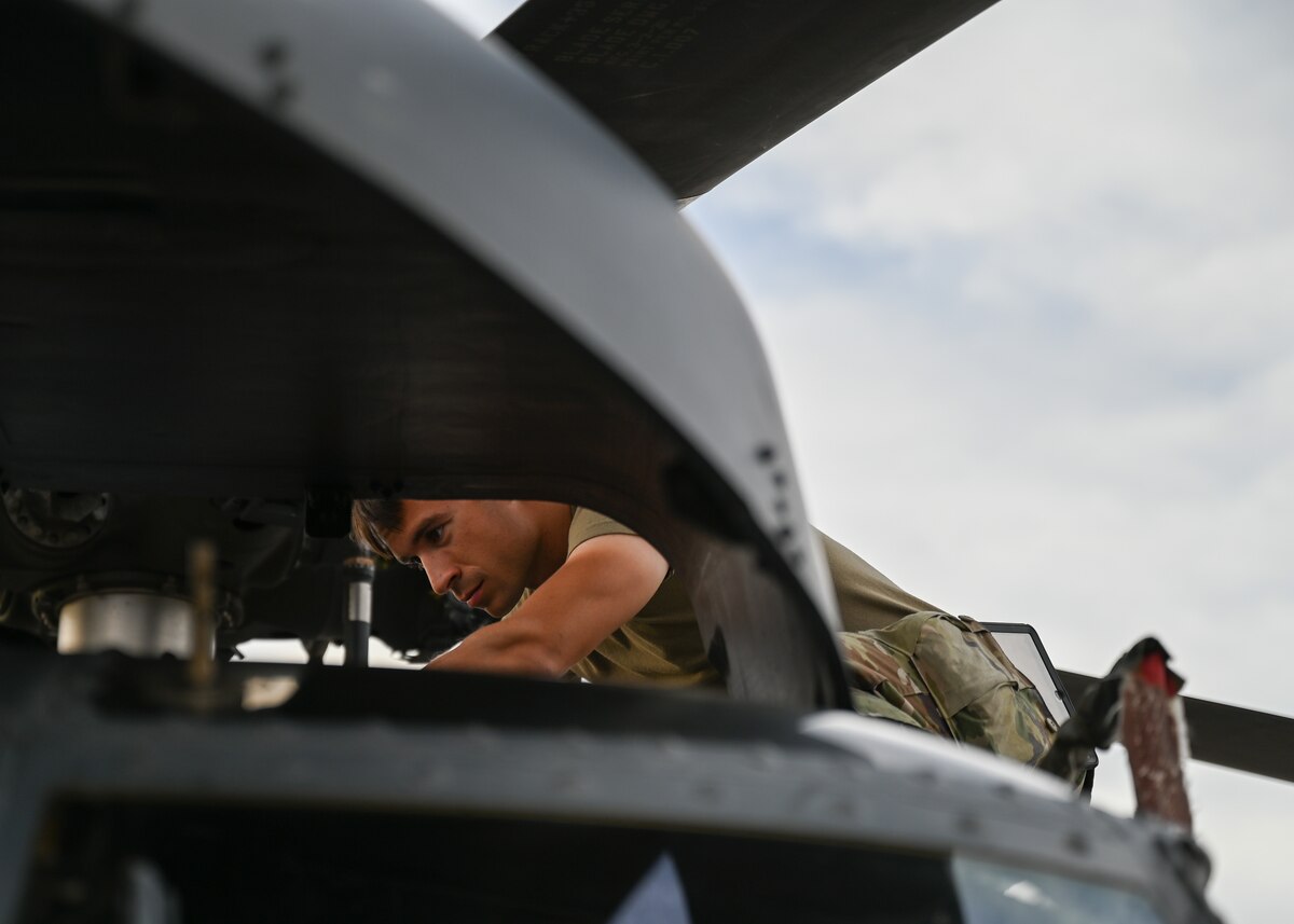 A man in a military uniform works on the top of a helicopter.
