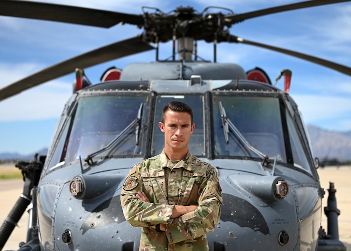 A man in a military uniform stands in front of a helicopter.