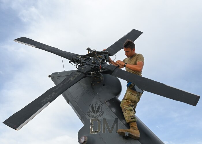 A man in a military uniform inspects the tail rotor on a helicopter.