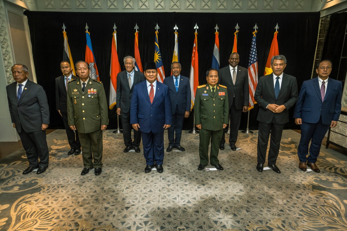 A group of men stand before a row of flags.