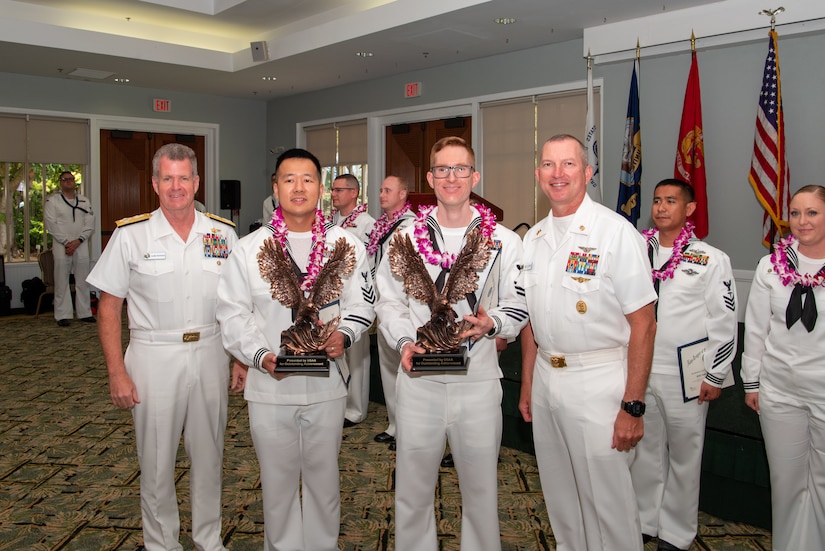 Four sailors pose for a photo while two hold trophies.