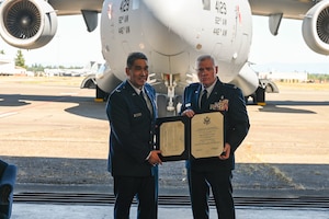 Two people dressed in their Air Force blue dress uniform hold a certificate in front of a C-17 Globemaster III.