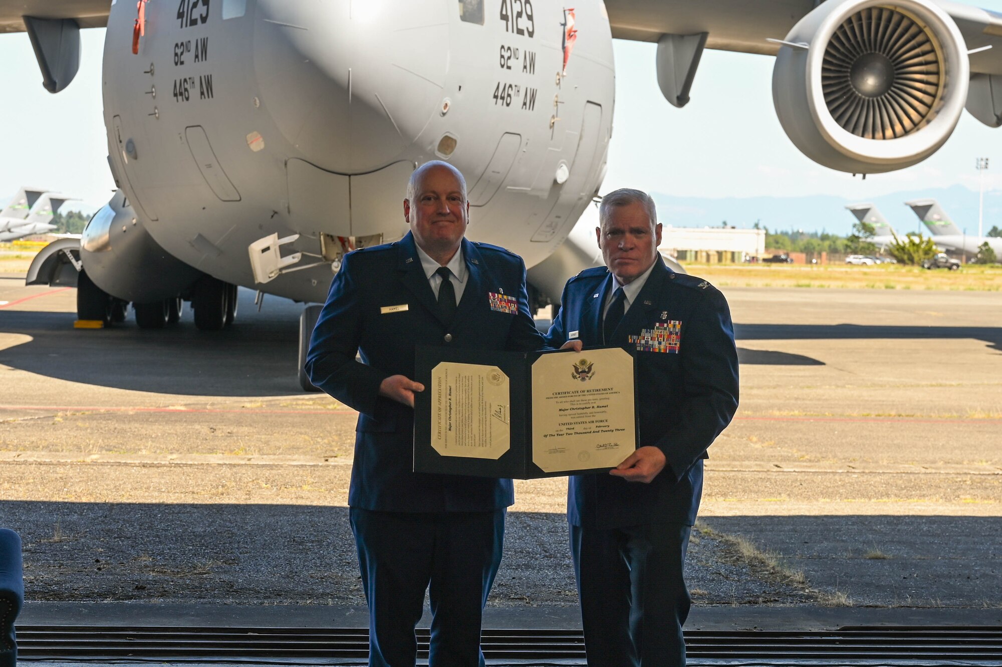 Two people dressed in their Air Force blue dress uniform hold a certificate in front of a C-17 Globemaster III.