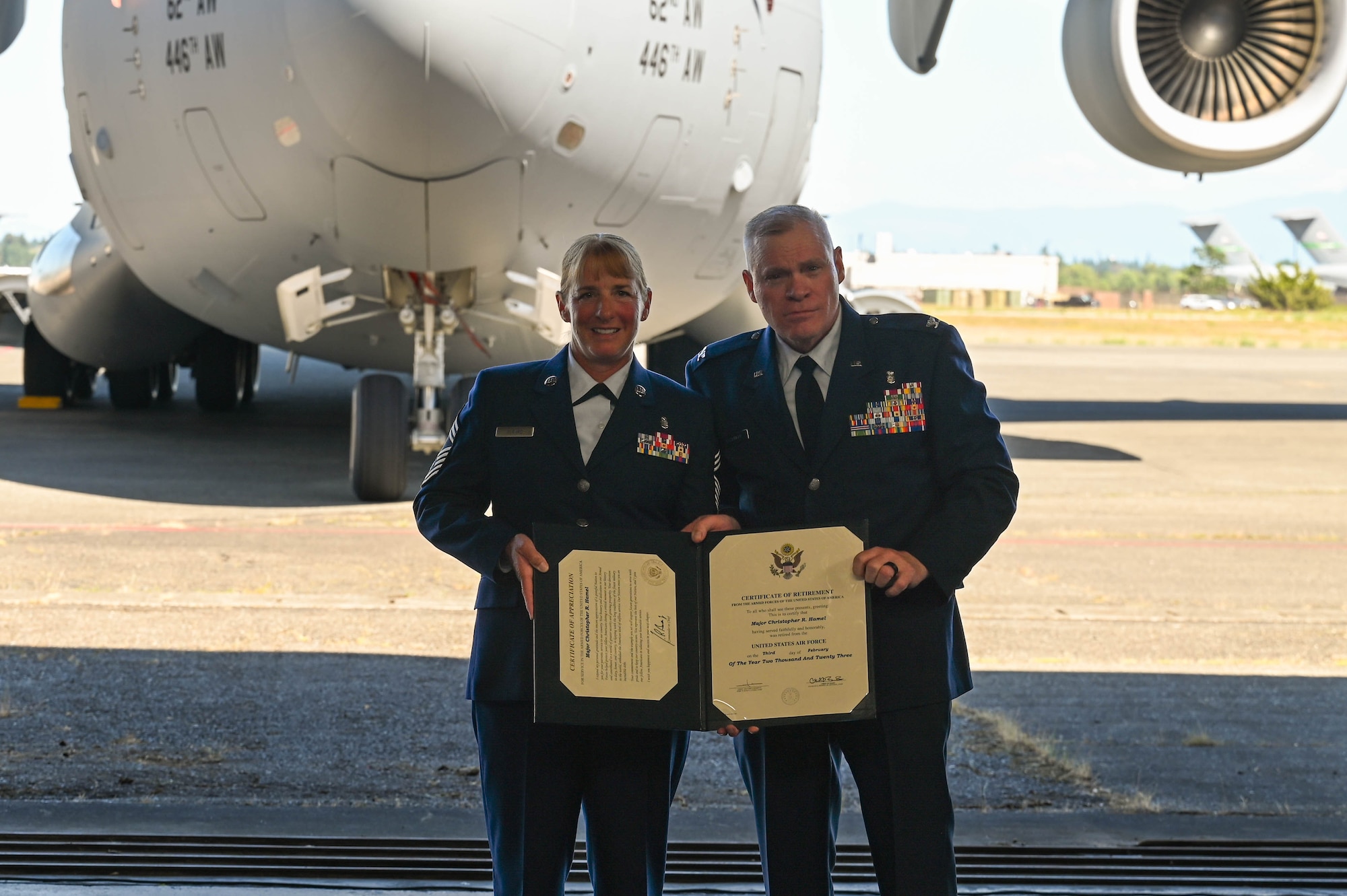 Two people dressed in their Air Force blue dress uniform hold a certificate in front of a C-17 Globemaster III.