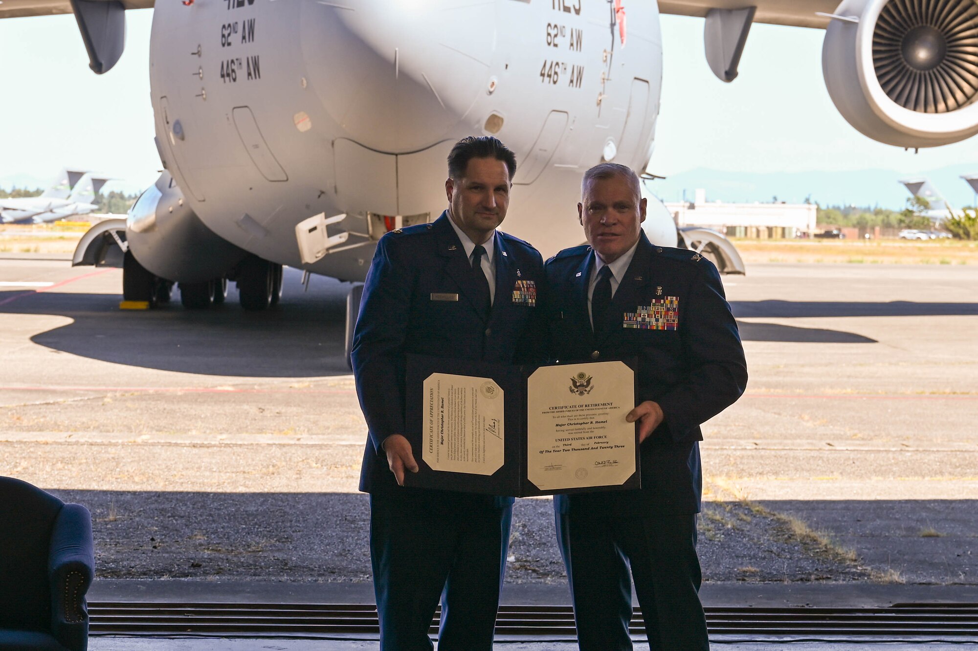 Two men dressed in their Air Force blue dress uniform hold a certificate in front of a C-17 Globemaster III.