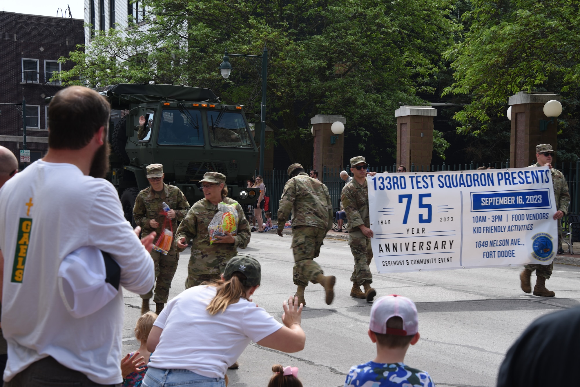 Airmen give treats to parade goers. Airmen hold event banner.