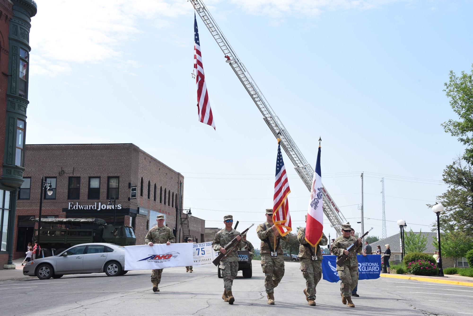 Airmen march under flag suspended by fire engine ladder.