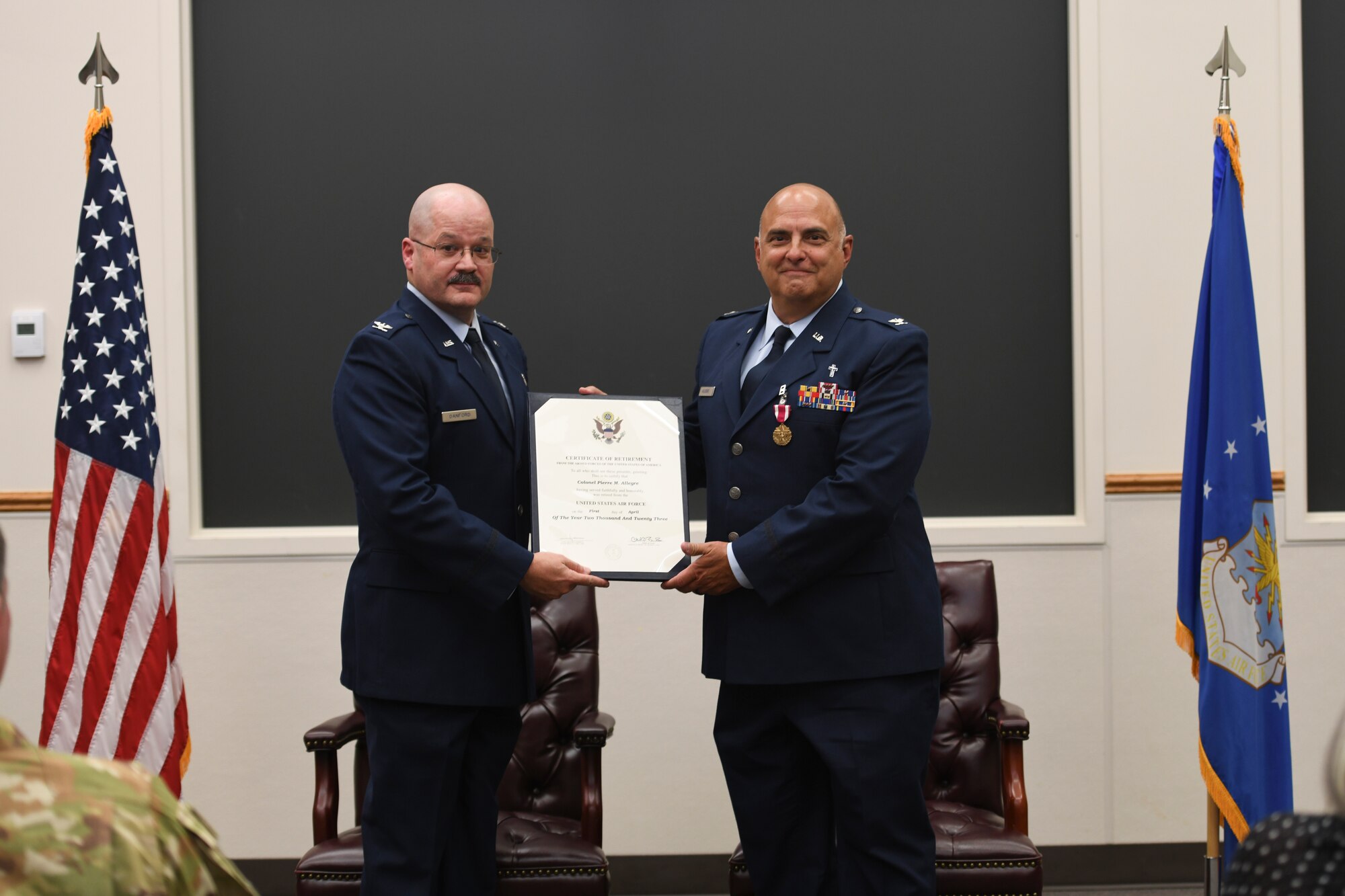 Two men dressed in Air Force dress uniforms standing in front of a room holding a certificate of retirement.