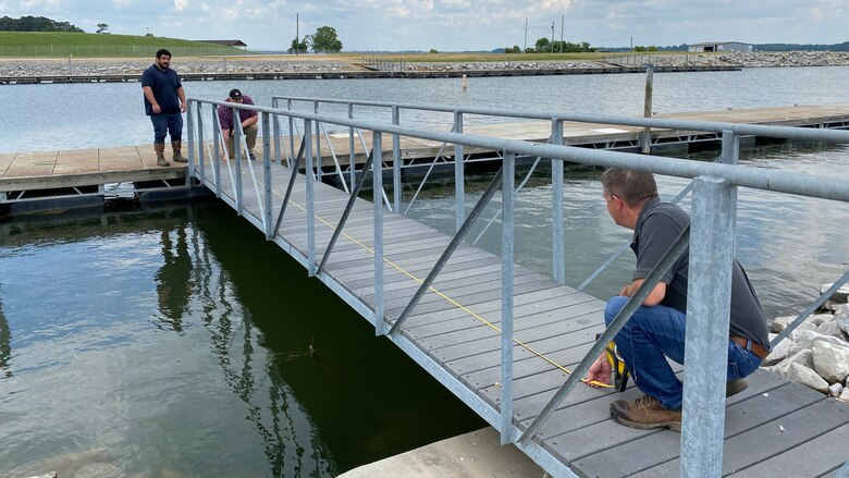 Three men stand on a boat dock and measure the length of the dock.