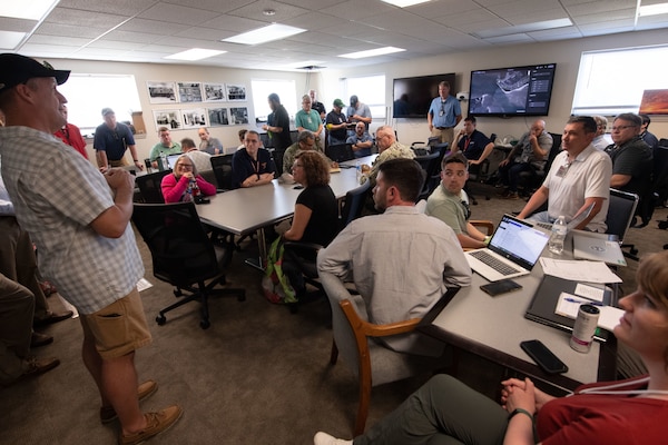 Team of people sitting at long desk in a room conducting a kick off brief for the week ling tresting event.