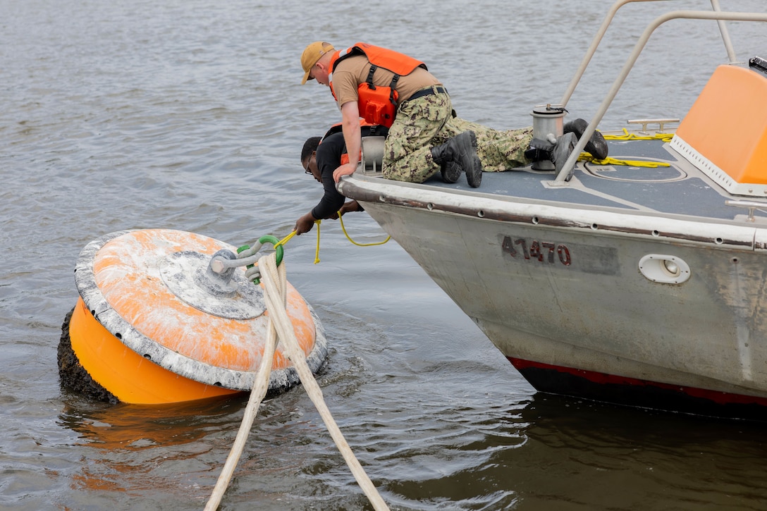 Sailors lean over the side of a boat to connect it to a buoy.