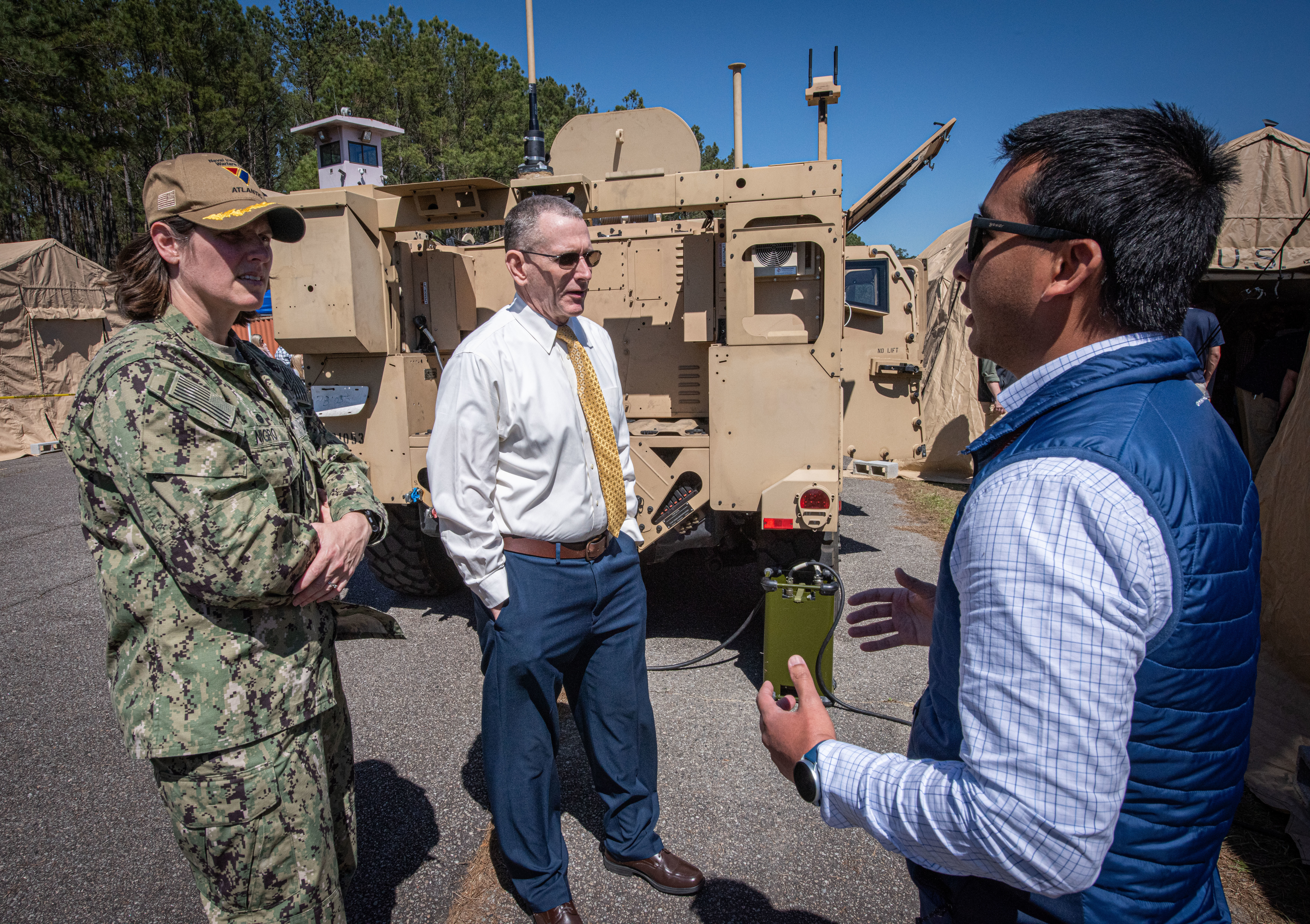 Commanding Officer and Executive Director listen as man to the right describes how equipment is used on the Joint Light Tactical Vehicle.