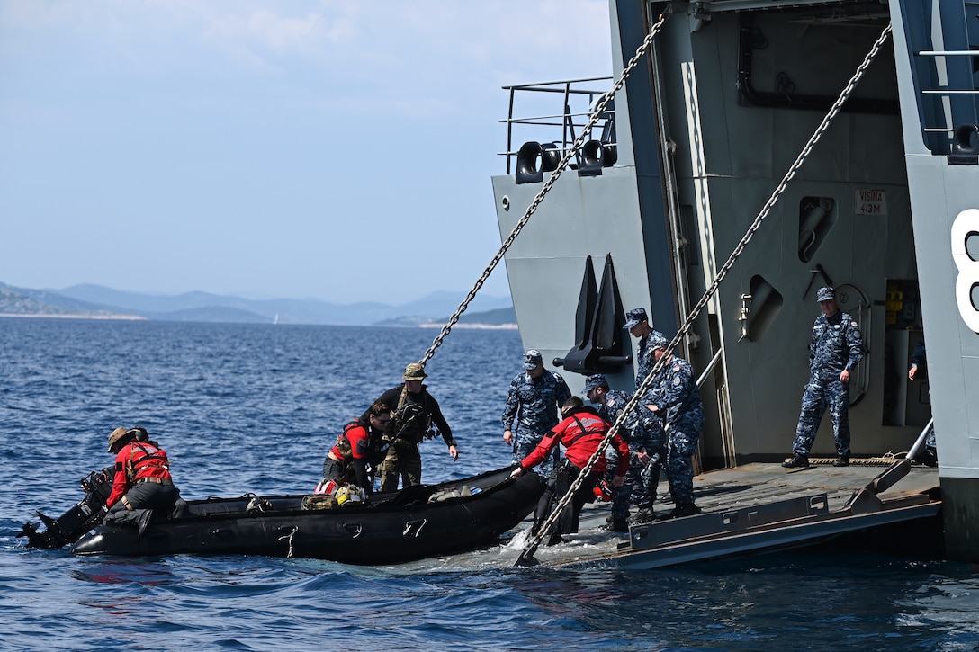 Airmen pull a boat on board a larger vessel.