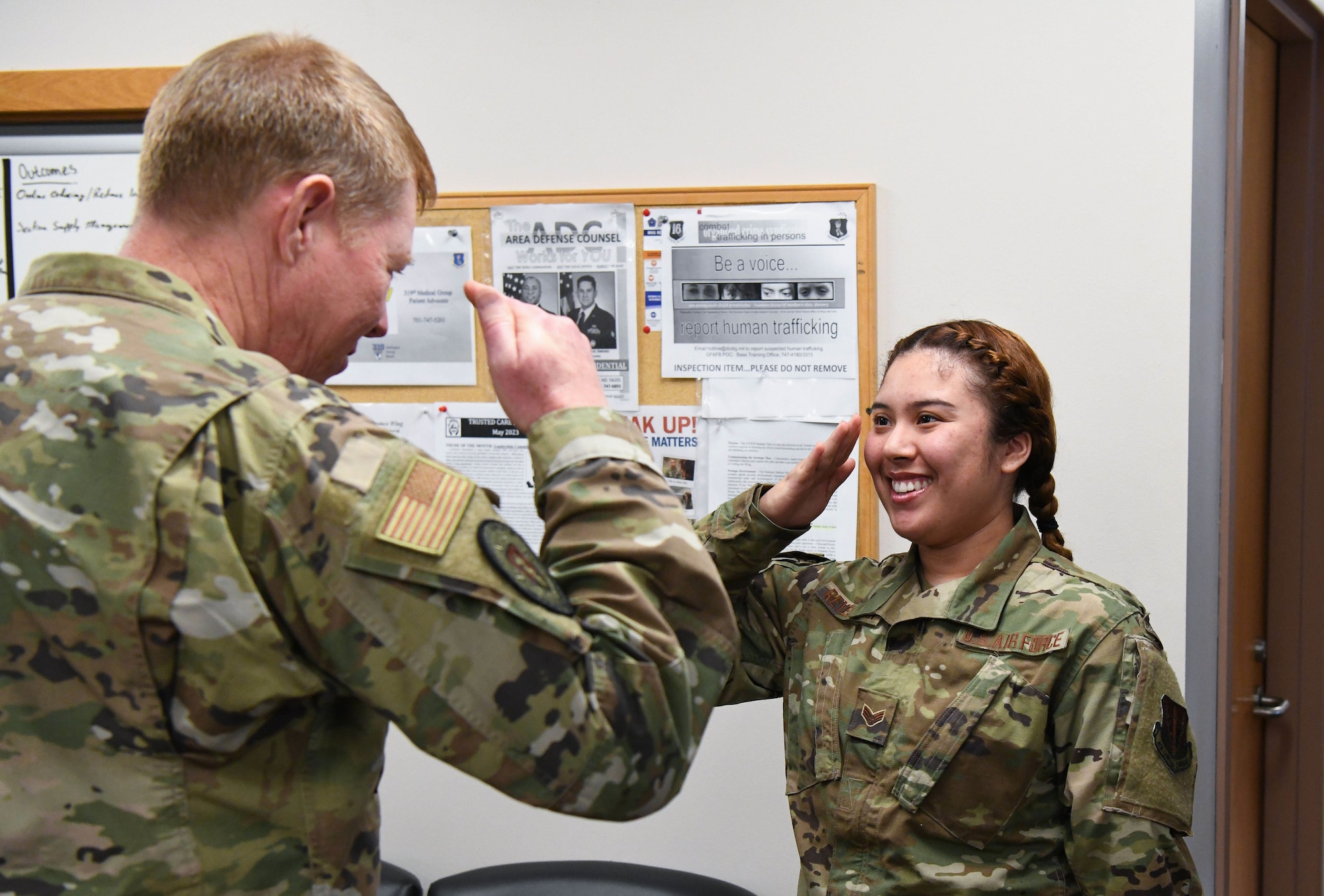Two individuals in military uniforms salute each other.