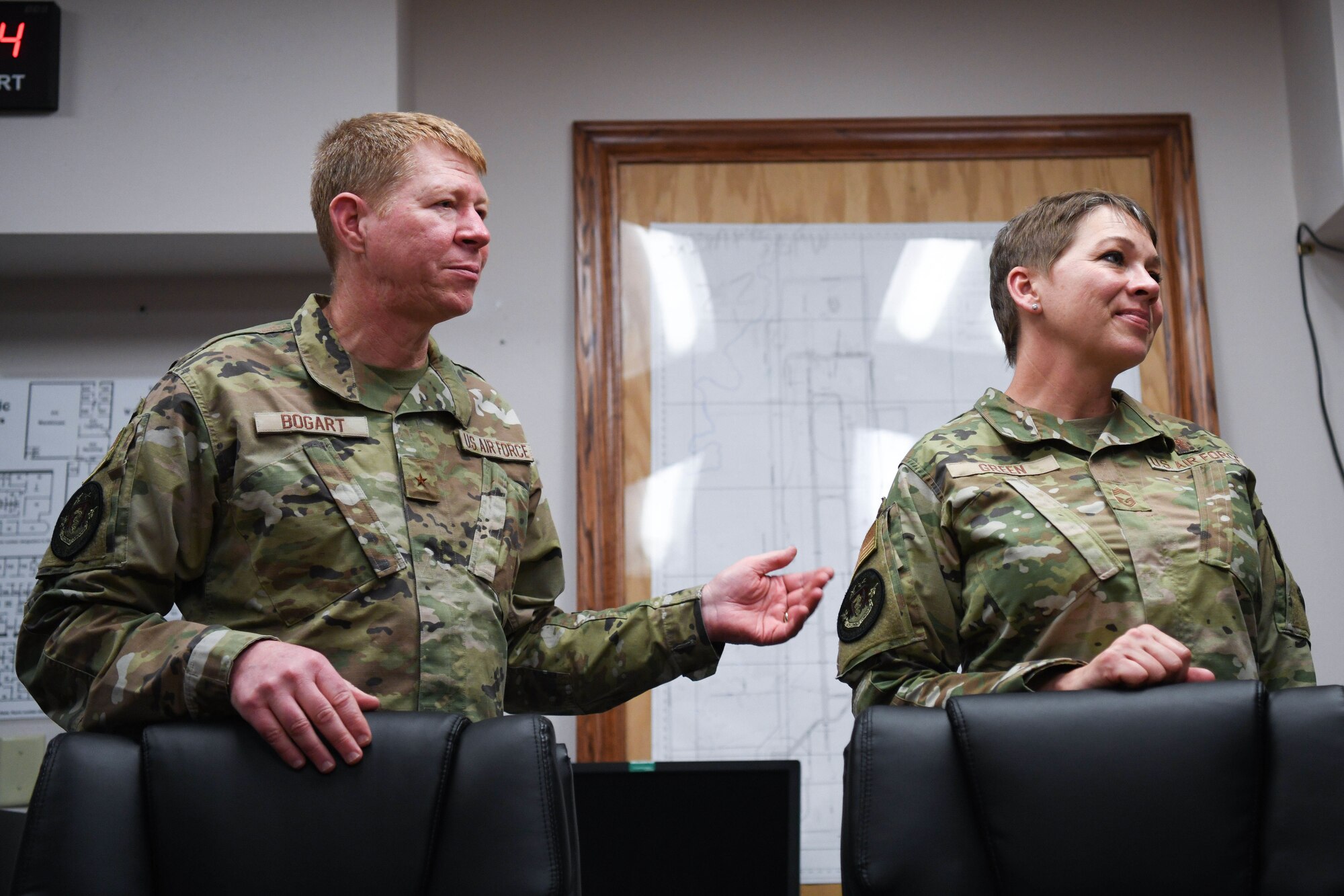 Two people in military uniforms stand in front of a table.