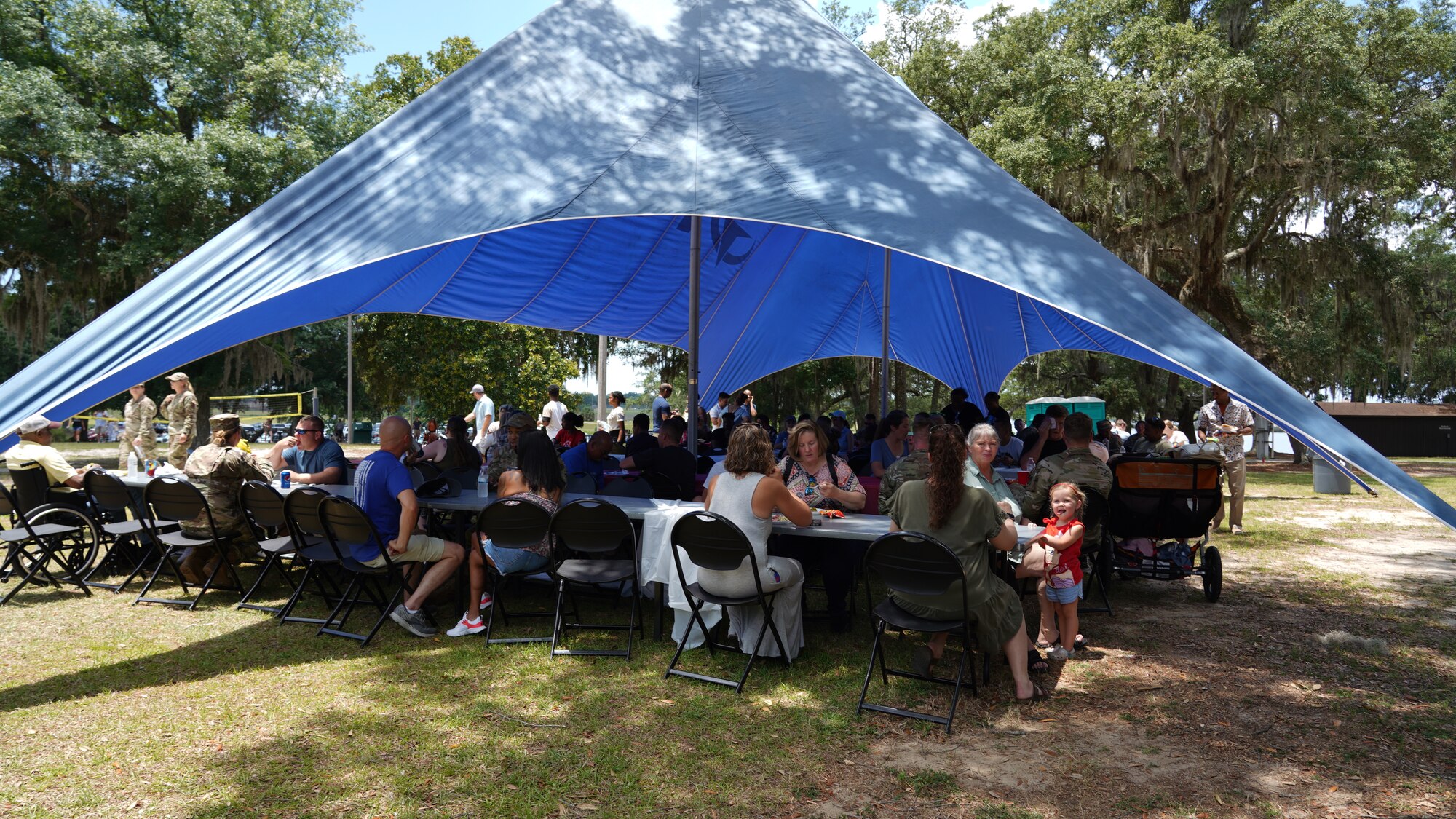 Wing members and their families sit under a tent eating during the family day celebration.