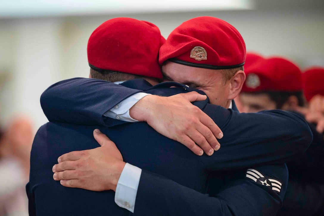 Two airmen wearing red berets hug each other.