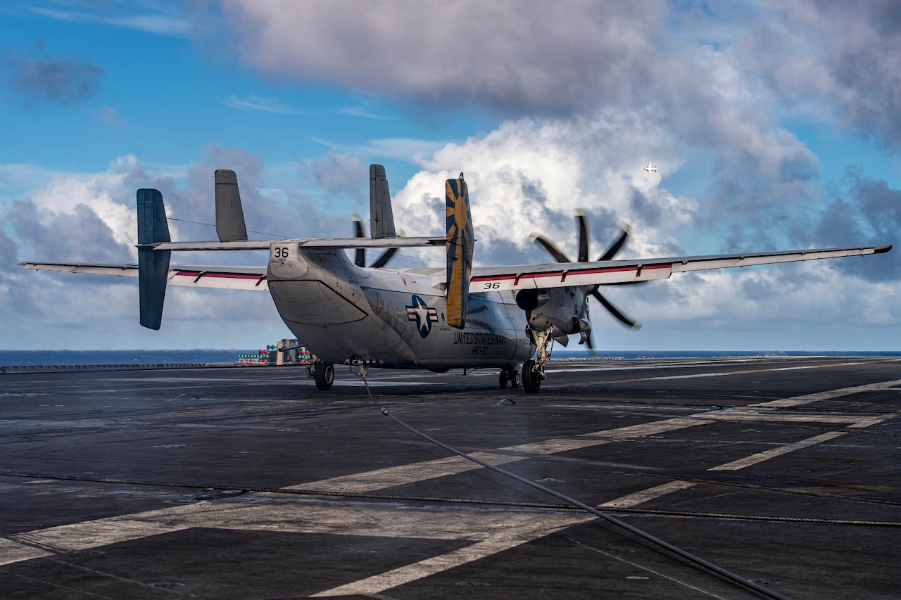 Rear-side view of an aircraft landing on the deck of a ship at sea.