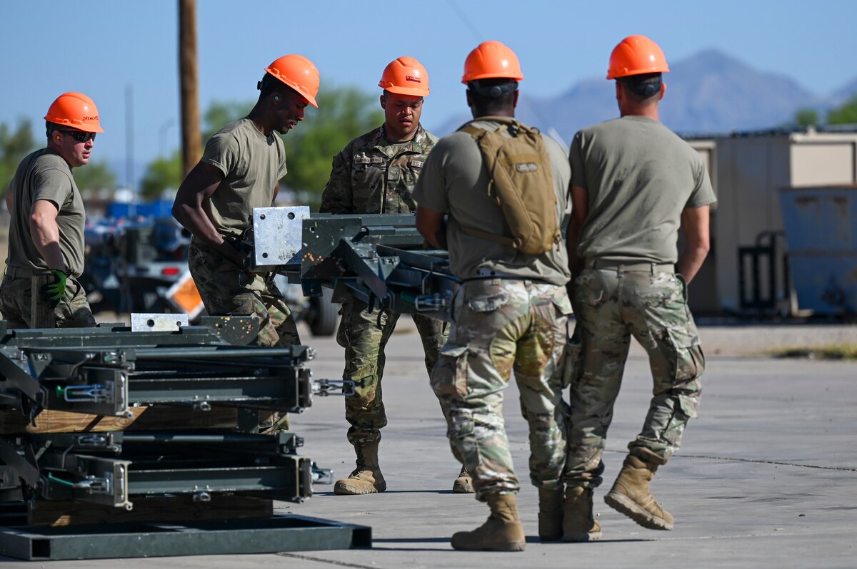 A photo of a group of people in military uniforms carrying part of a munitions assembly conveyor.